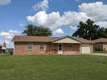 Burkburnett house for rent - a brick house with a green lawn and a cloudy sky