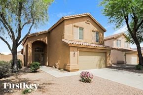 Peoria house for rent - A house with a brown stucco exterior and a tan roof is surrounded by trees and has a gravel driveway.