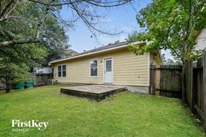 Spring house for rent - A small house with a porch is surrounded by a fence and trees.