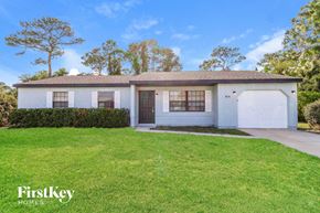 Palm Bay house for rent - A white house with a brown roof and a garage door is surrounded by a green lawn.
