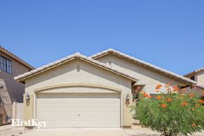 Peoria house for rent - A house with a garage door and a tree with orange flowers in front.