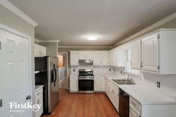 Stockbridge house for rent - a kitchen with white cabinets and black appliances and a wooden floor