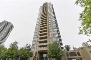 Burnaby apartment for rent - A tall residential building with balconies on the upper floors stands in front of other buildings and trees.