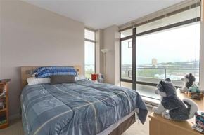 Burnaby apartment for rent - A bedroom with a large bed and a window overlooking a cityscape.