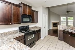 Fort Worth house for rent - a kitchen with wood cabinets and black appliances and granite counter tops
