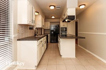Houston house for rent - a kitchen with white cabinets and black counter tops