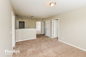 Charlotte house for rent - A spacious room with beige carpeting and white walls, with a door on the left and a window on the right.