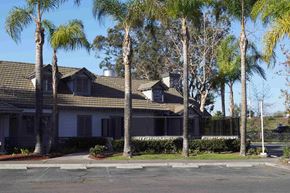Artesia apartment for rent - A building with a brown roof and white walls is surrounded by palm trees.