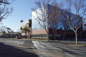Artesia apartment for rent - A modern building with a glass facade is surrounded by trees.