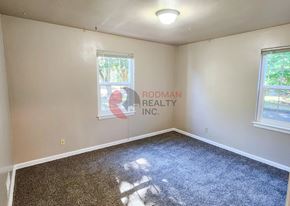 Longview apartment for rent - A room with a carpeted floor and a window with a view of trees and a building outside.
