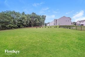 Monroe house for rent - A grassy field with trees and a house in the background.