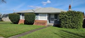 Longview house for rent - A house with a grey roof and a grey door is surrounded by green grass.