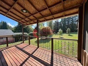 Longview house for rent - A wooden deck with a railing and a view of a green lawn and trees.