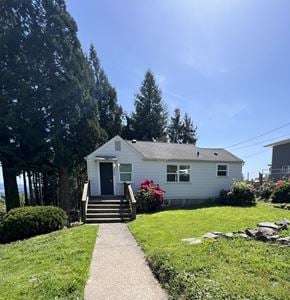 Longview house for rent - A small white house with a grey roof and a grey door is surrounded by greenery.