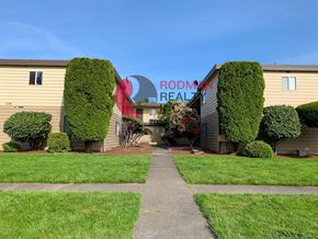 Longview apartment for rent - A building with a sign that says "Rodman Realty" is surrounded by green bushes and trees.