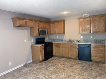 Lenexa apartment for rent - a kitchen with wooden cabinets and a black stove and dishwasher