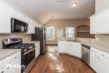 Spring house for rent - a kitchen with white cabinets and stainless steel appliances and wood floors