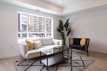 Winnipeg apartment for rent - A living room with a white couch, a glass coffee table, and a black chair with a yellow pillow.