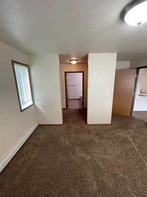 Fargo apartment for rent - an empty living room with carpeting and a hallway with a door to a bedroom