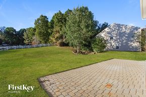 Waxhaw house for rent - A brick walkway leads to a house with a white fence and green trees in the background.