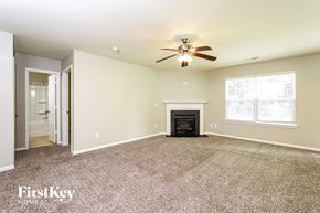 Kernersville house for rent - A carpeted room with a fireplace and a ceiling fan.