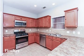 Cypress house for rent - A kitchen with red cabinets and stainless steel appliances.