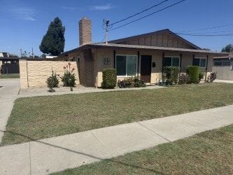 Garden Grove apartment for rent - A house with a brown roof and a chimney is surrounded by a lawn and a sidewalk.