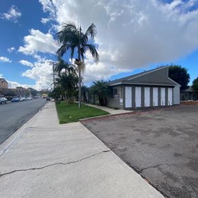 National City apartment for rent - A building with a grey roof is situated on a street with a sidewalk and a palm tree.