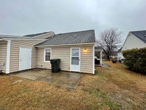 Wilson apartment for rent - A house with a brown roof and a white door is surrounded by a grassy area.