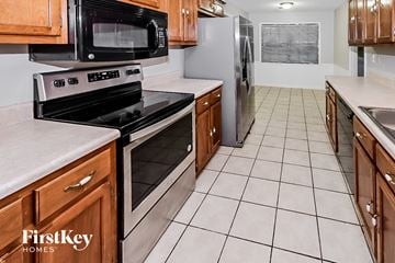 Bartlett house for rent - a kitchen with wood cabinets and black appliances and white tiled floor