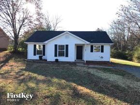 Monroe house for rent - A small white house with a black roof is surrounded by grass and trees.