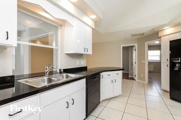 North Port house for rent - a kitchen with white cabinets and black counter tops and a sink