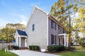 Greensboro house for rent - A house with a grey facade and a white door is surrounded by greenery.
