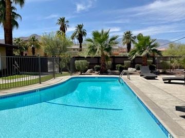 Cathedral City apartment for rent - A swimming pool surrounded by a fence and palm trees.