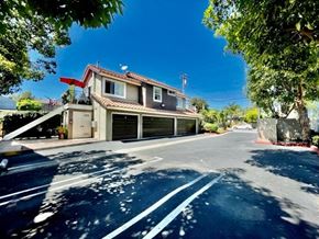 Costa Mesa apartment for rent - A two-story house with a garage is surrounded by trees and has a clear blue sky above.