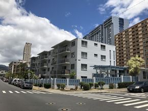 Honolulu apartment for rent - A street view of a residential area with cars parked on the side of the road and modern buildings in the background.