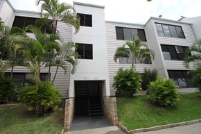 Waianae apartment for rent - A white building with a black door and windows surrounded by greenery.