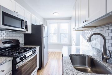 Allston apartment for rent - a kitchen with white cabinets and black appliances and granite counter tops