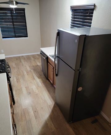 Hemet house for rent - A black refrigerator in a kitchen with wooden floors and a window with blinds.