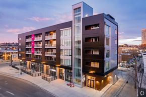 Calgary apartment for rent - A modern multi-story building with a glass facade and a pink banner on the left side.