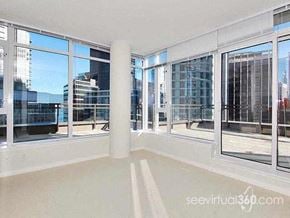 Vancouver apartment for rent - A sunny day in a spacious room with large windows overlooking a cityscape.