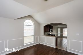 Forney house for rent - A large empty room with a window and a kitchen area in the background.