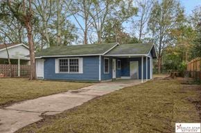 Hattiesburg house for rent - A blue house with a white fence and trees in the background.