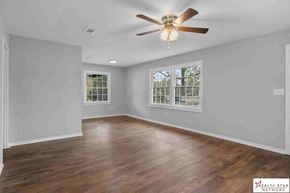 Hattiesburg house for rent - A spacious room with a ceiling fan and wooden flooring.