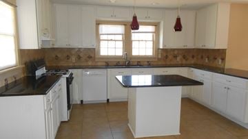 Hattiesburg house for rent - a large kitchen with white cabinets and black counter tops
