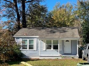 Hattiesburg house for rent - A small house with a white door and windows is surrounded by trees.