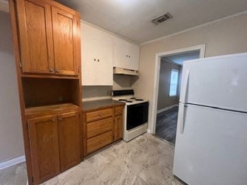 Hattiesburg house for rent - A kitchen with a white fridge, wooden cabinets and a window.
