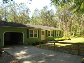 Seminary house for rent - the front of a green house with a driveway and trees