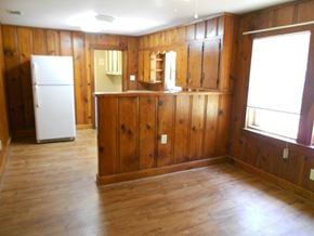 Seminary house for rent - an empty living room with wood paneling and a refrigerator