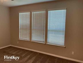 Haslet house for rent - A room with a carpeted floor and three windows covered in white blinds.